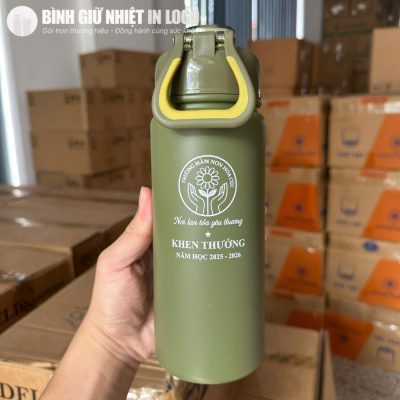 Cận cảnh nắp khóa thông minh và quai xách màu vàng nổi bật trên nền bình xanh Olive