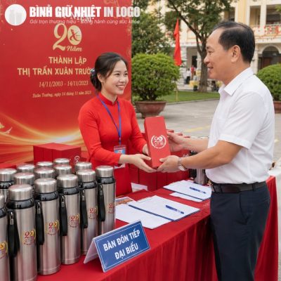 Khu vực bàn tiếp đón đại biểu ngoài trời trưng bày hàng loạt bình giữ nhiệt inox in logo và hộp quà đỏ
