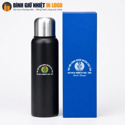 Bình giữ nhiệt màu đen nhám đứng cạnh hộp quà giấy cứng cáp màu xanh dương