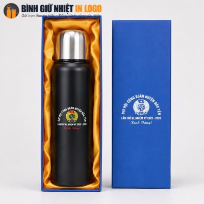 Bình giữ nhiệt đen nhám được đặt ngay ngắn trong khay lót lụa vàng của hộp quà