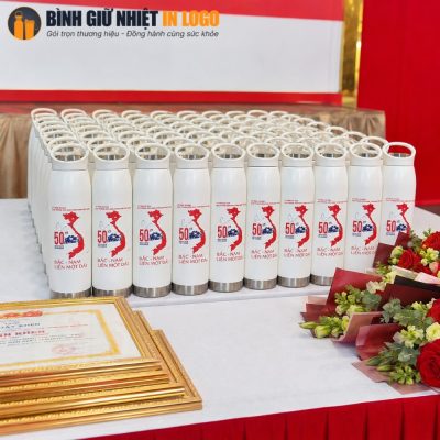 Hàng trăm chiếc bình nước in họa tiết kỷ niệm được xếp ngay ngắn trên bàn sự kiện bên cạnh khung bằng khen