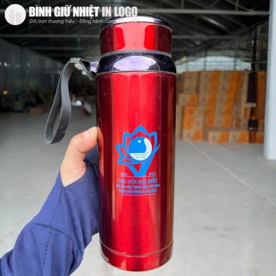 Cận cảnh chiếc bình giữ nhiệt màu đỏ phủ bóng in logo sắc nét được cầm chắc chắn trên tay