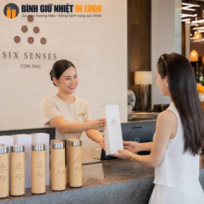 Nhân viên resort trao tặng hộp quà chứa bình giữ nhiệt vỏ tre khắc logo cho khách hàng tại quầy lễ tân.