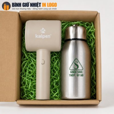 Cận cảnh bên trong hộp carton lót rơm xanh lá chứa quạt mini Kalpen màu kem và bình inox 304 in logo Thép Tây Đô