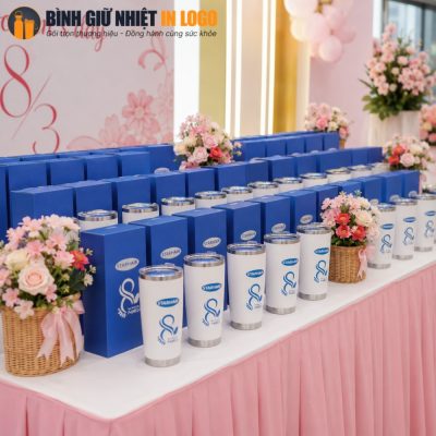 Hàng cốc giữ nhiệt trắng và hộp quà màu xanh dương được xếp ngay ngắn trên bàn tiệc sự kiện 8/3